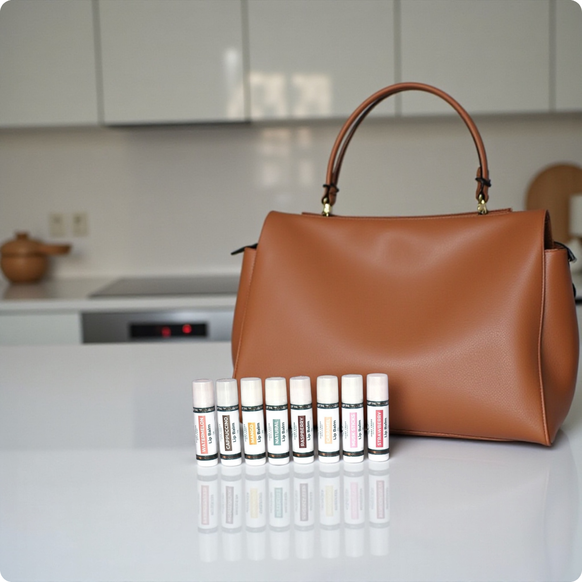 8 lip balm tubes stand on a counter in front of a brown leather handbag.
